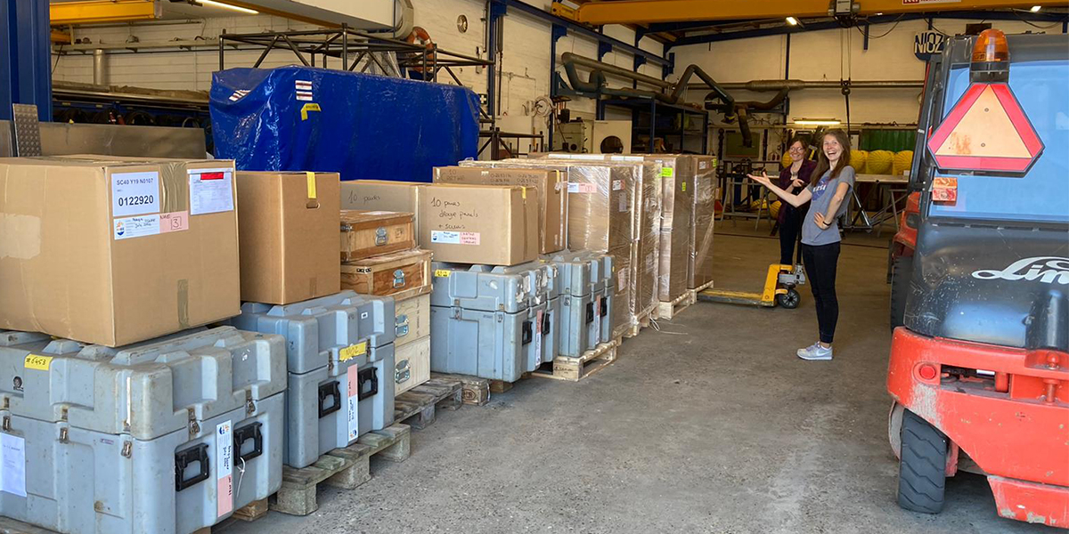 Nora Fried and Elodie Duyck face a wall of boxes with surface drifters, ADCPs and other mooring equipment.